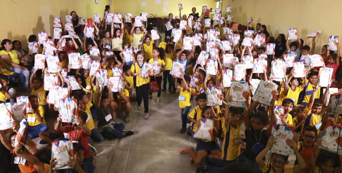 Crianças levantando kits com brindes depois da palestra do projeto CDF