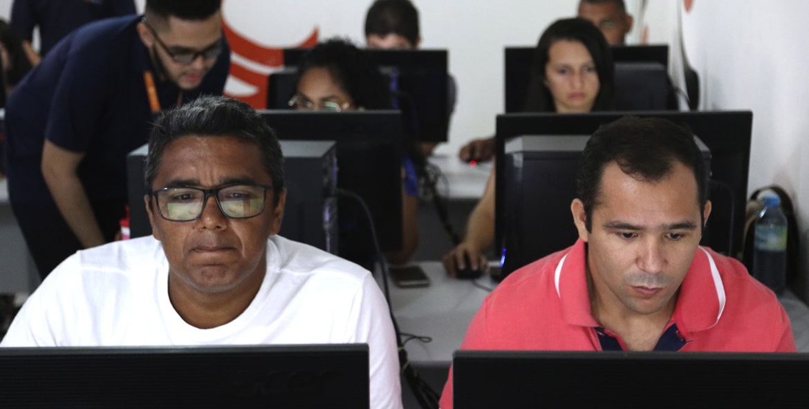 Sala com vários alunos estudando em computadores