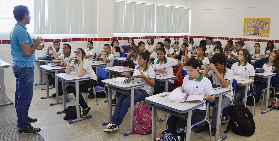 Sala de aula com alunos concentrados na explicação do professor